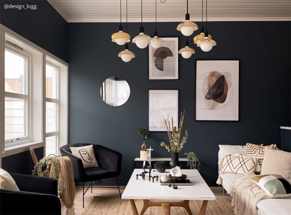 Dnevni boravak s tamnim zidovima, crni baršunasti fotelji, okruglo zrcalo, grafičke slike